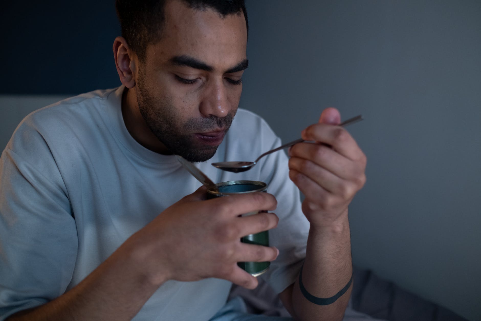man wearing white shirt eating canned food